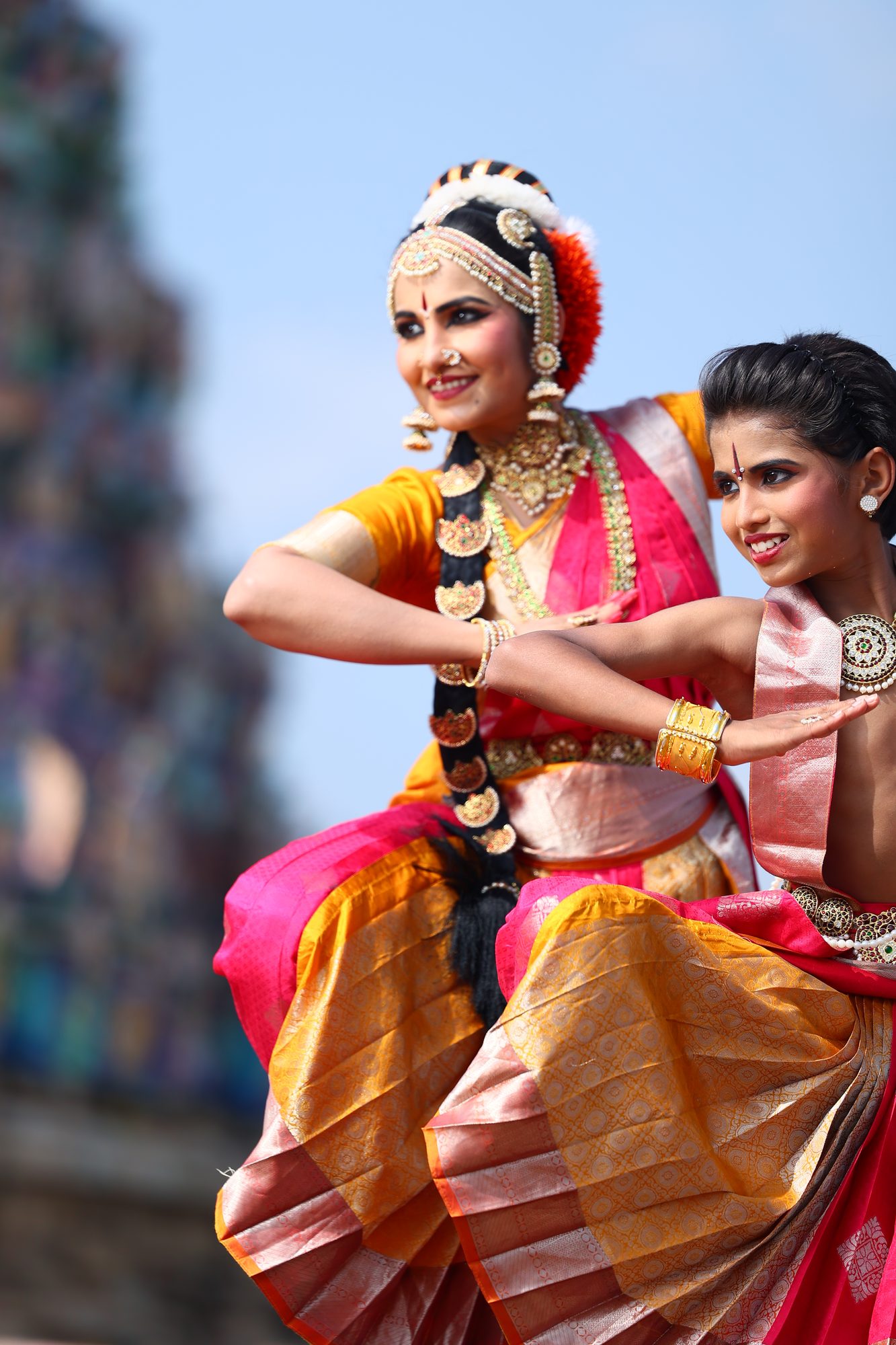 Smt. Pooja Raj dancing alongside a student, a temple gopuram behind them
